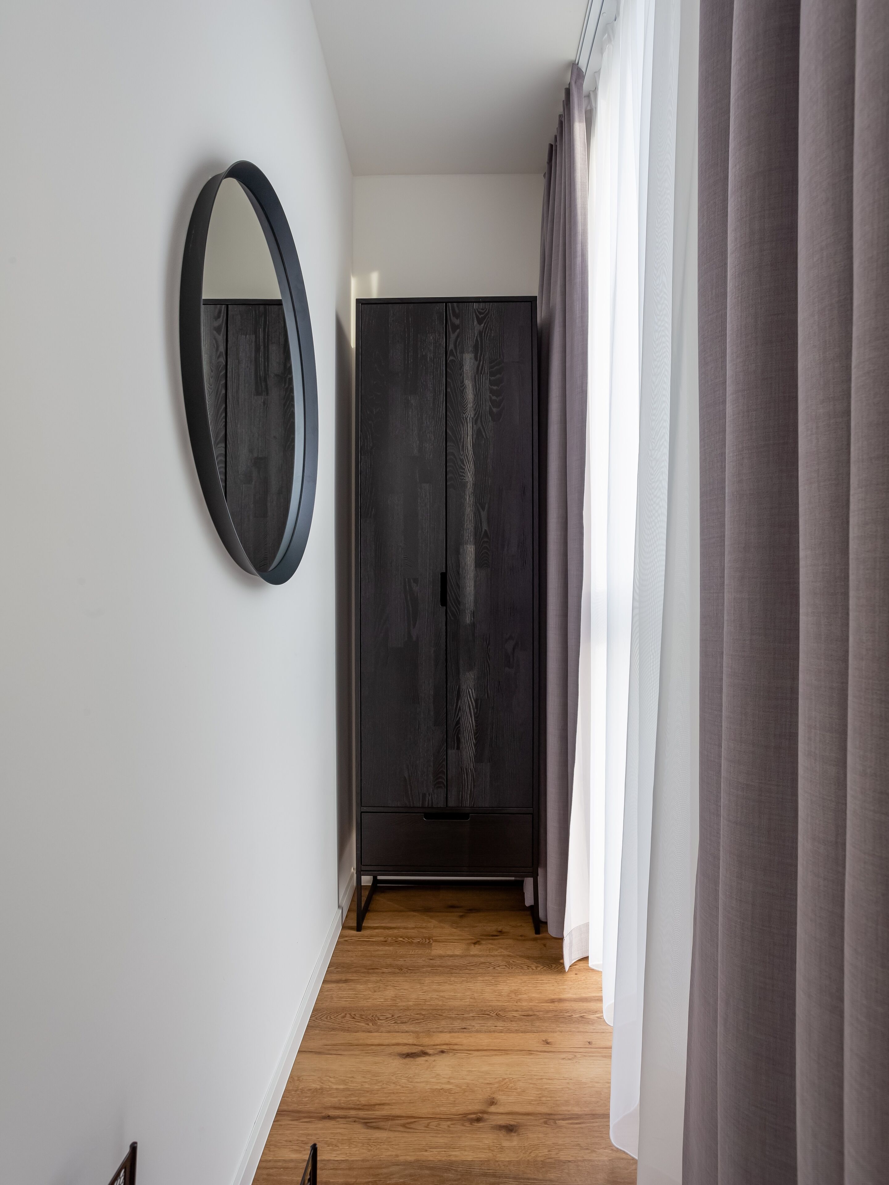 Un pasillo con suelo de madera, un armario oscuro y un espejo redondo en la pared.