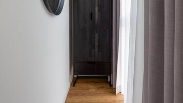 A hallway with a wooden floor, a dark wardrobe, and a round mirror on the wall.