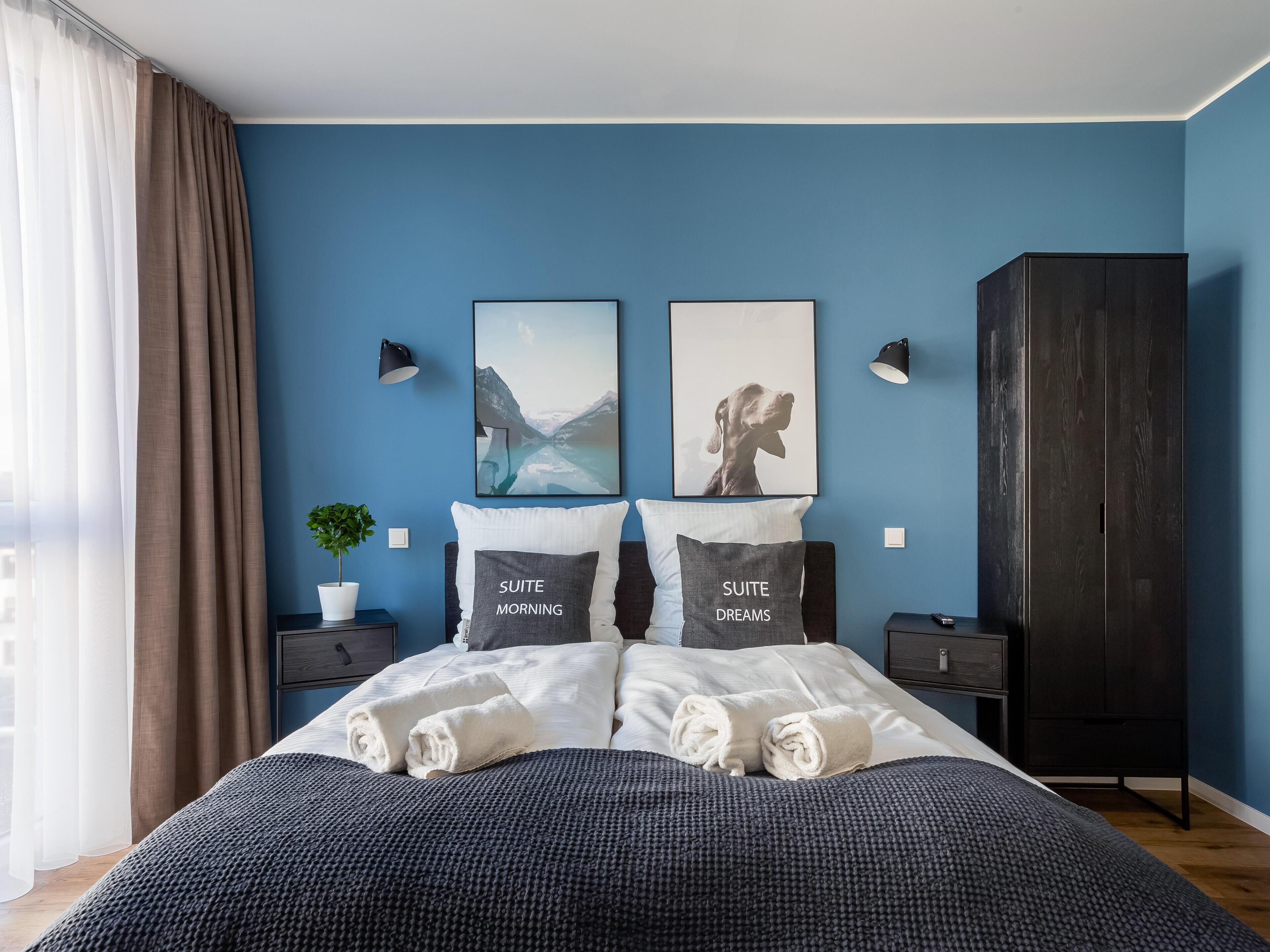 A modern bedroom with a bed, two pillows, a nightstand, a potted plant, and a wardrobe.
