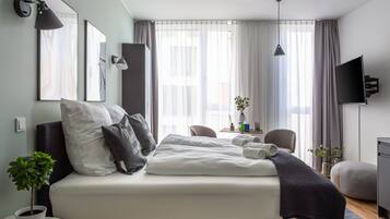 A modern hotel room with a large bed, bedside tables, a desk, and a TV.