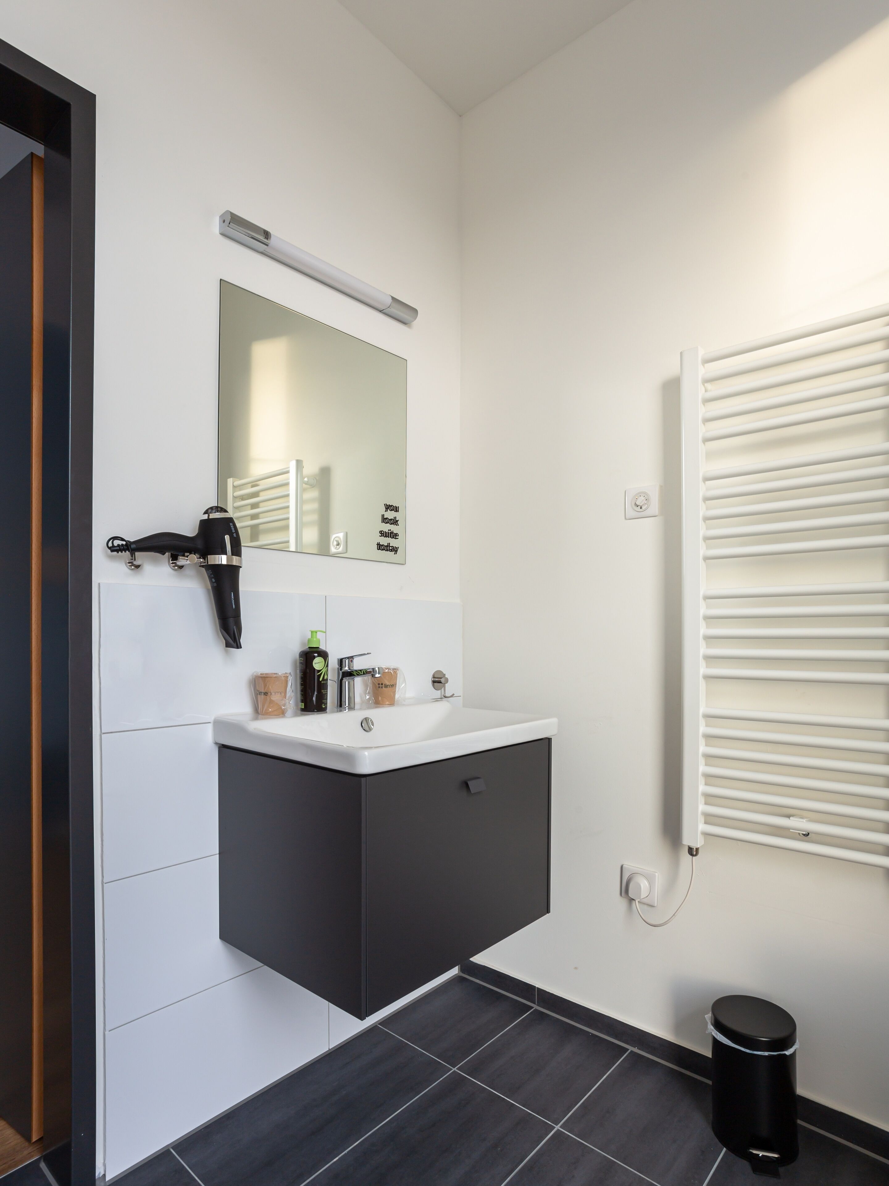 A modern bathroom with a white vanity, a mirror, a hairdryer, and a radiator.