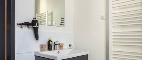 A modern bathroom with a white vanity, a mirror, a hairdryer, and a radiator.