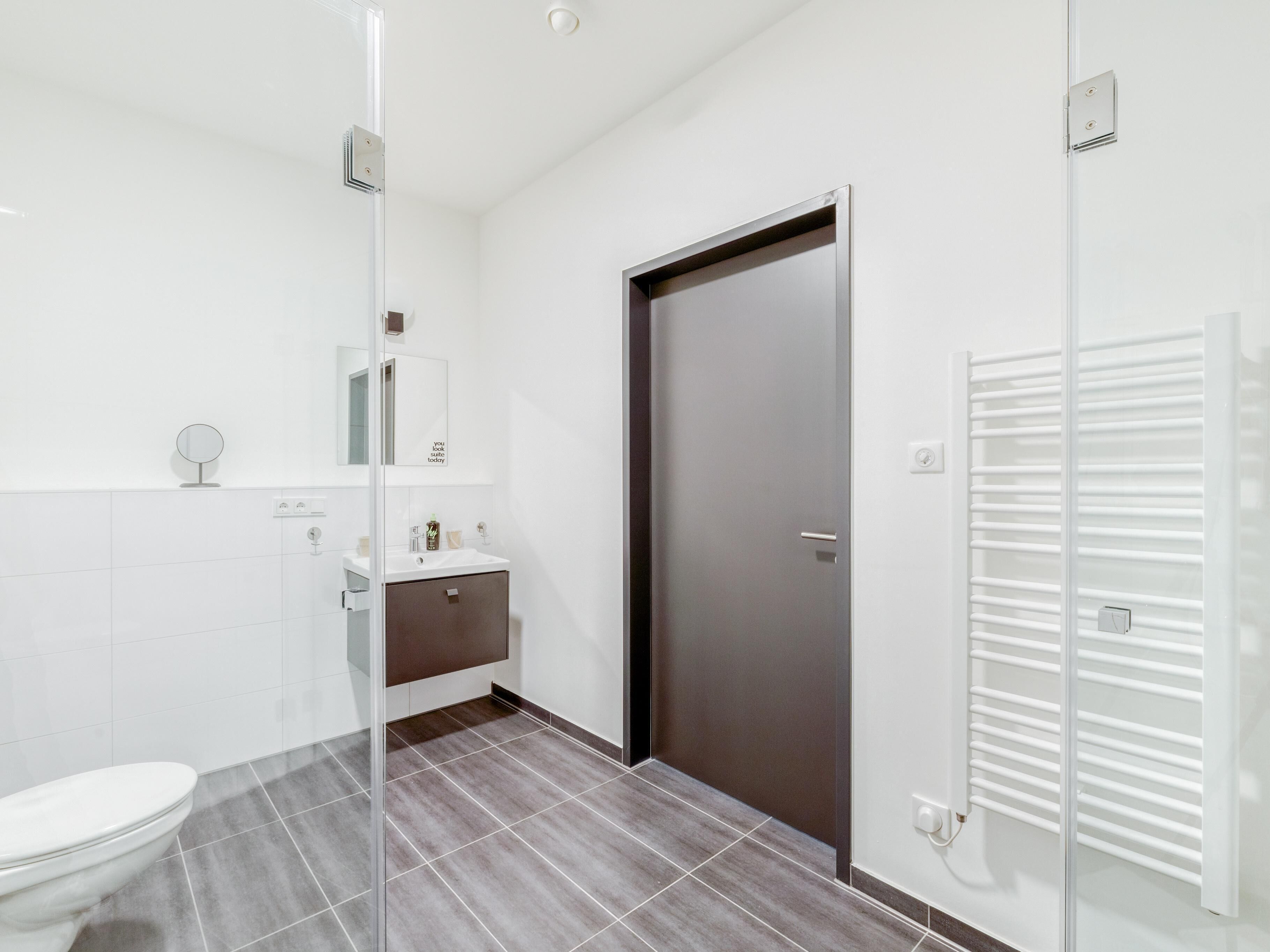 Ein modernes Badezimmer mit Toilette, Waschbecken, Spiegel und Duschkabine aus Glas.