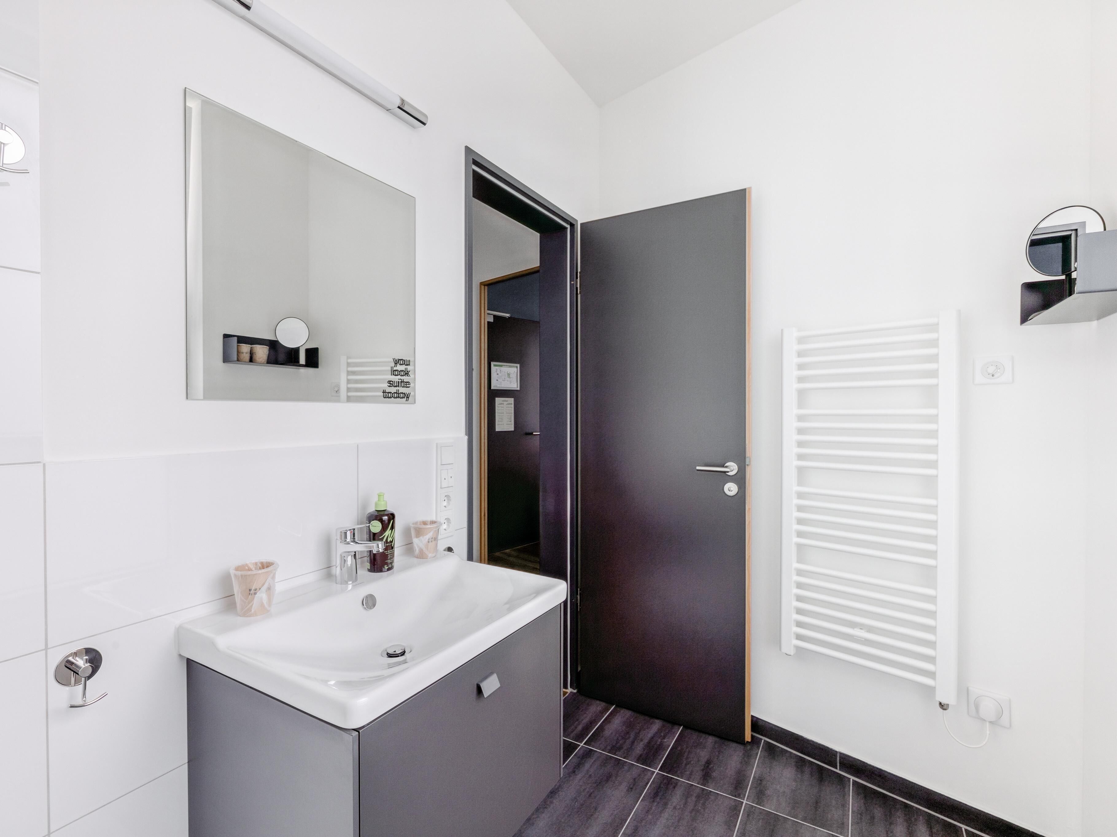 A modern bathroom with a white sink, dark cabinet, and a mirror above it.