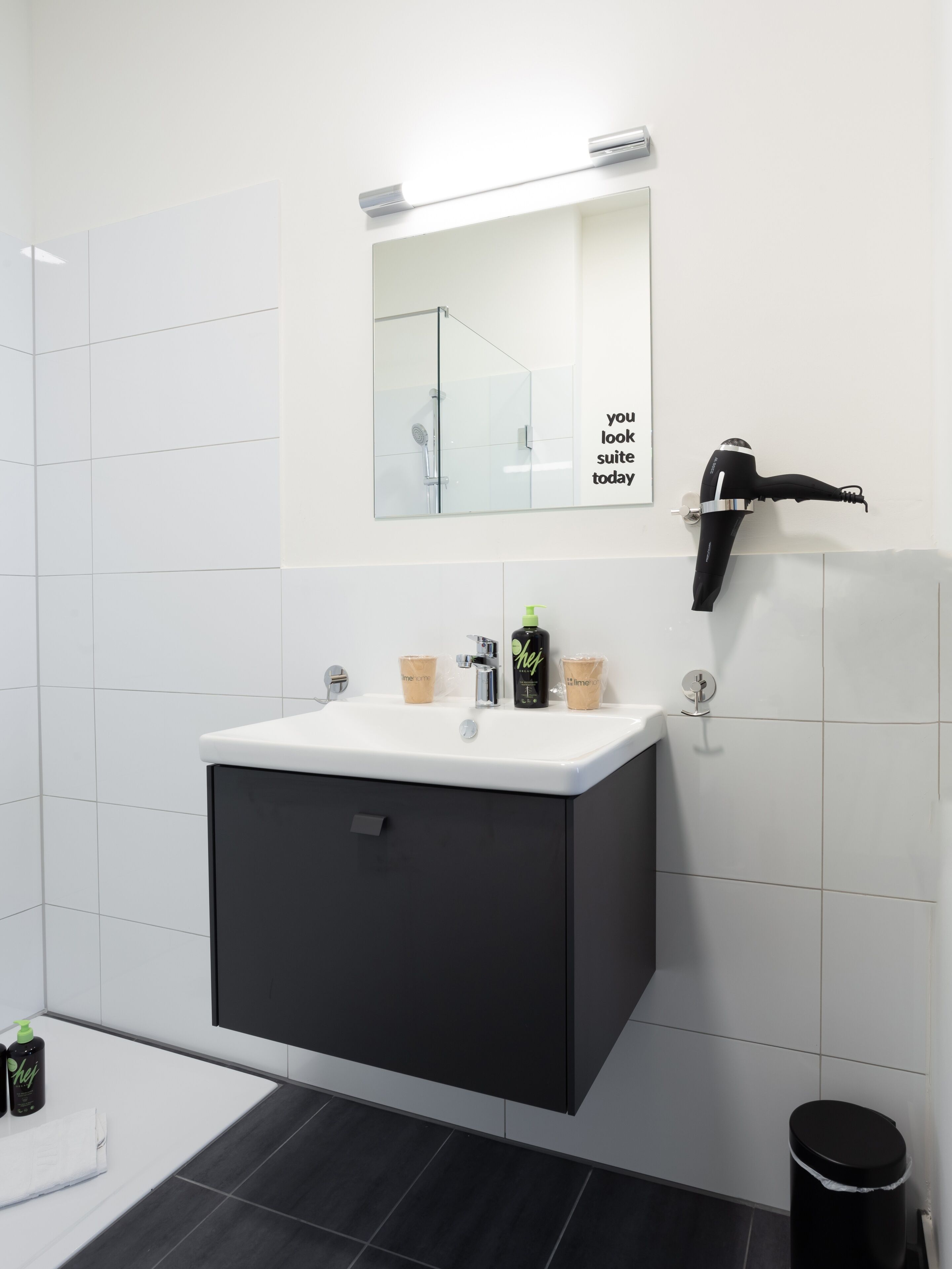 Une salle de bain moderne avec un meuble-lavabo blanc, un miroir et un sèche-cheveux noir fixé au mur.