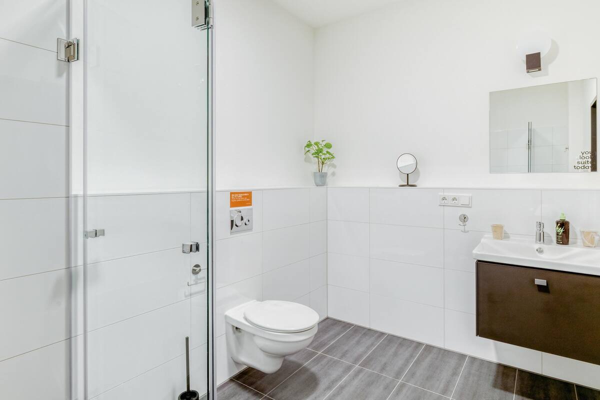 Un bagno moderno con cabina doccia in vetro, un water bianco, un lavabo con specchio e una pianta in vaso.
