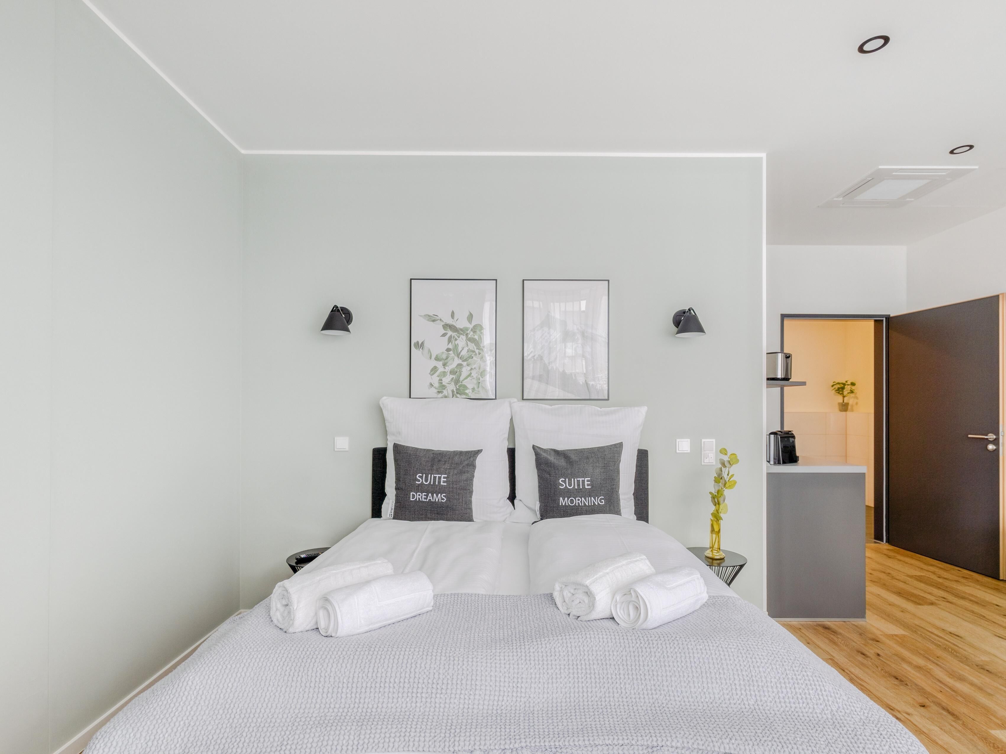 Una habitación de hotel moderna con una cama grande, dos mesitas de noche, un escritorio y una puerta que da a un baño.