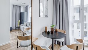 A modern living room with a round table, grey chairs, and a large window with grey curtains. - Limehome Mönchengladbach Fliethstraße (Moenchengladbach)