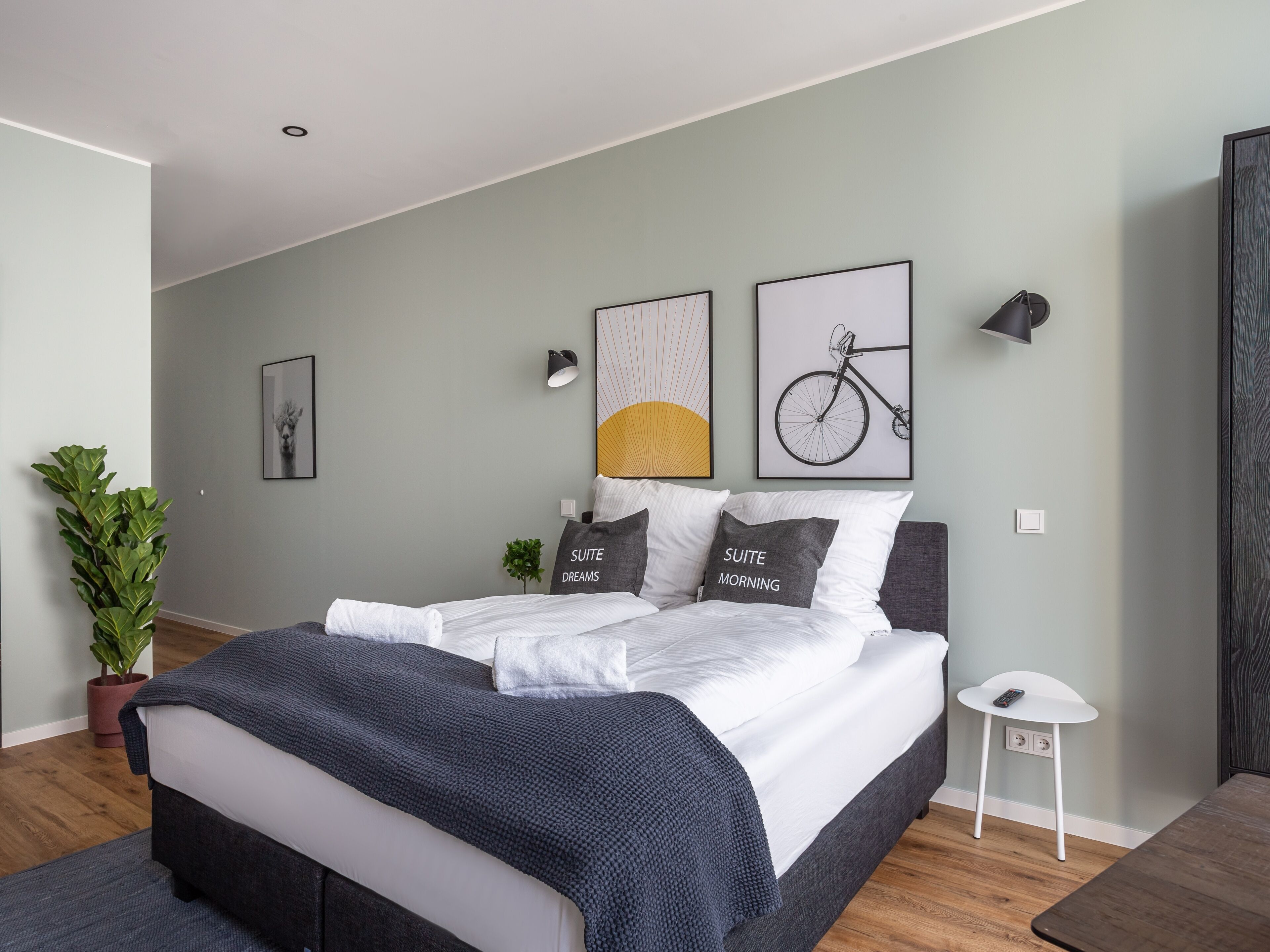A modern bedroom with a bed, a potted plant, and artwork on the walls.