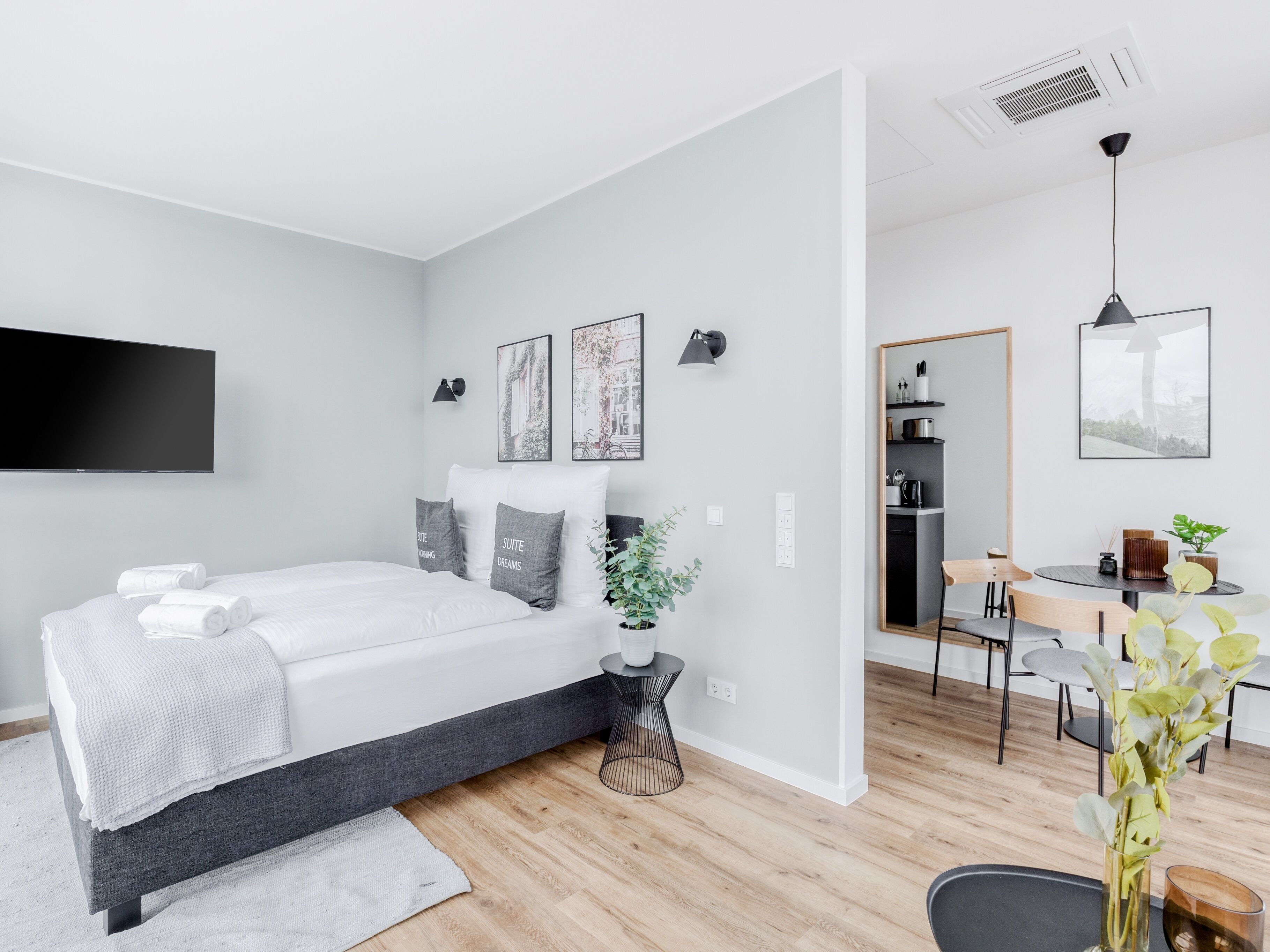 A modern bedroom with a bed, bedside tables, a TV, and a dining area with chairs and a table.