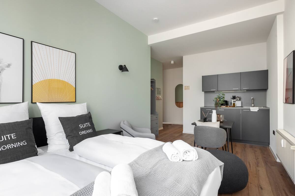 A modern hotel room with a large bed, a small kitchenette, and a view of the hallway.