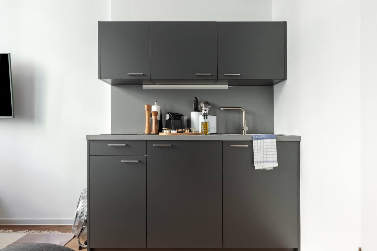 A modern kitchen with grey cabinets, a built-in oven, and a sink.