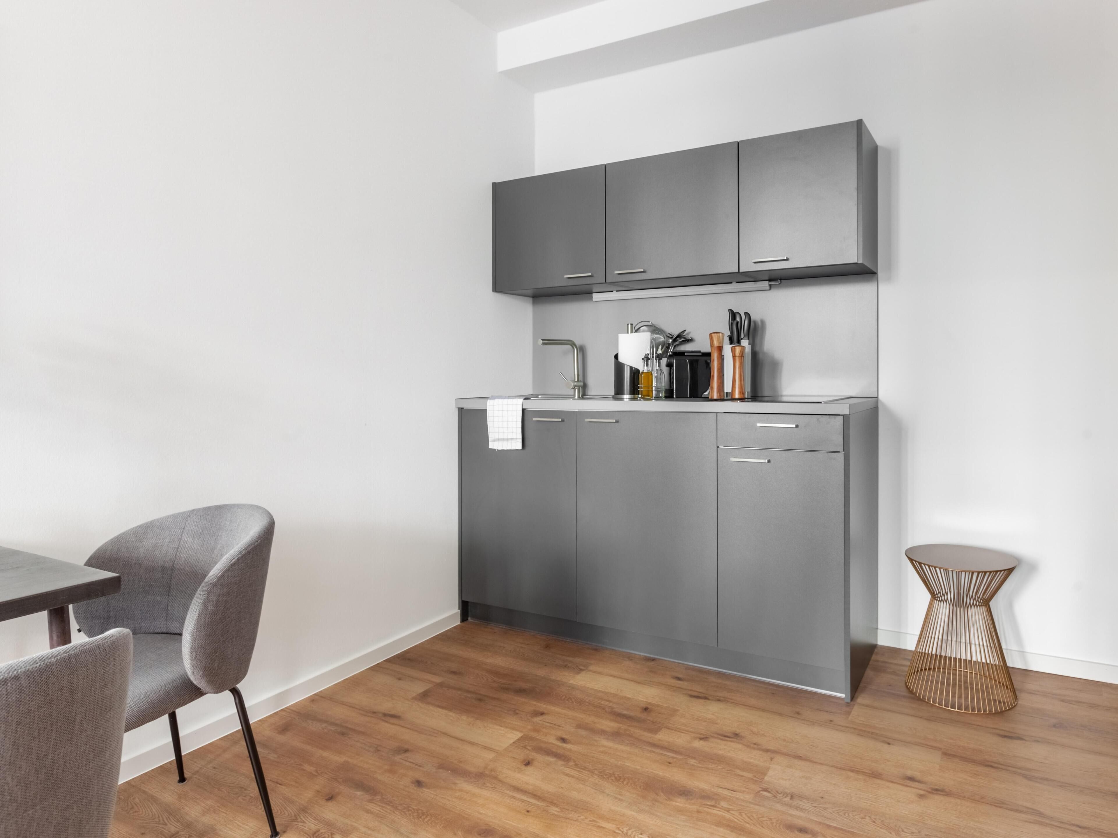 A modern kitchen with grey cabinets, a wooden floor, and a dining area with grey chairs.