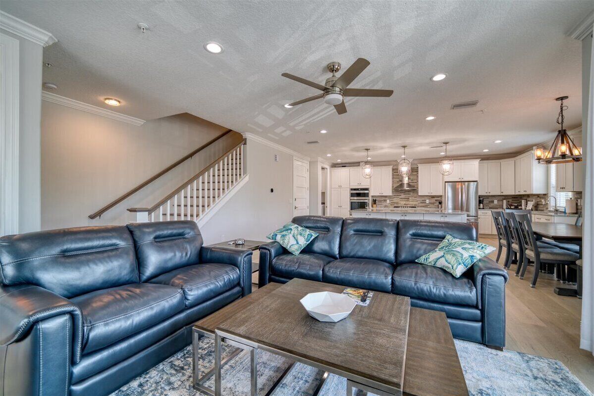 A spacious living room with a dark leather sectional sofa, a wooden coffee table, and a ceiling fan.