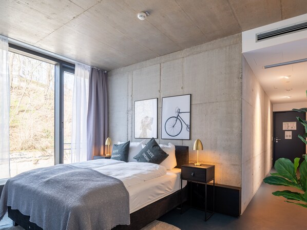A modern bedroom with a large bed, a nightstand, a lamp, and a window with curtains. - Limehome Erfurt Maximilian-Welsch-Str. (Erfurt)