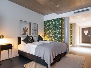 A modern bedroom with a large bed, a nightstand, and a wall with a leafy pattern. - Limehome Erfurt Maximilian-Welsch-Str. (Erfurt)