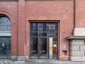 A red brick building with a large glass door and a small window. - Limehome Erfurt Maximilian-Welsch-Str. (Erfurt)
