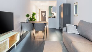 A modern living room with a flat-screen TV, a grey sofa, and a dining area with two chairs and a small table. - Limehome Erfurt Maximilian-Welsch-Str. (Erfurt)