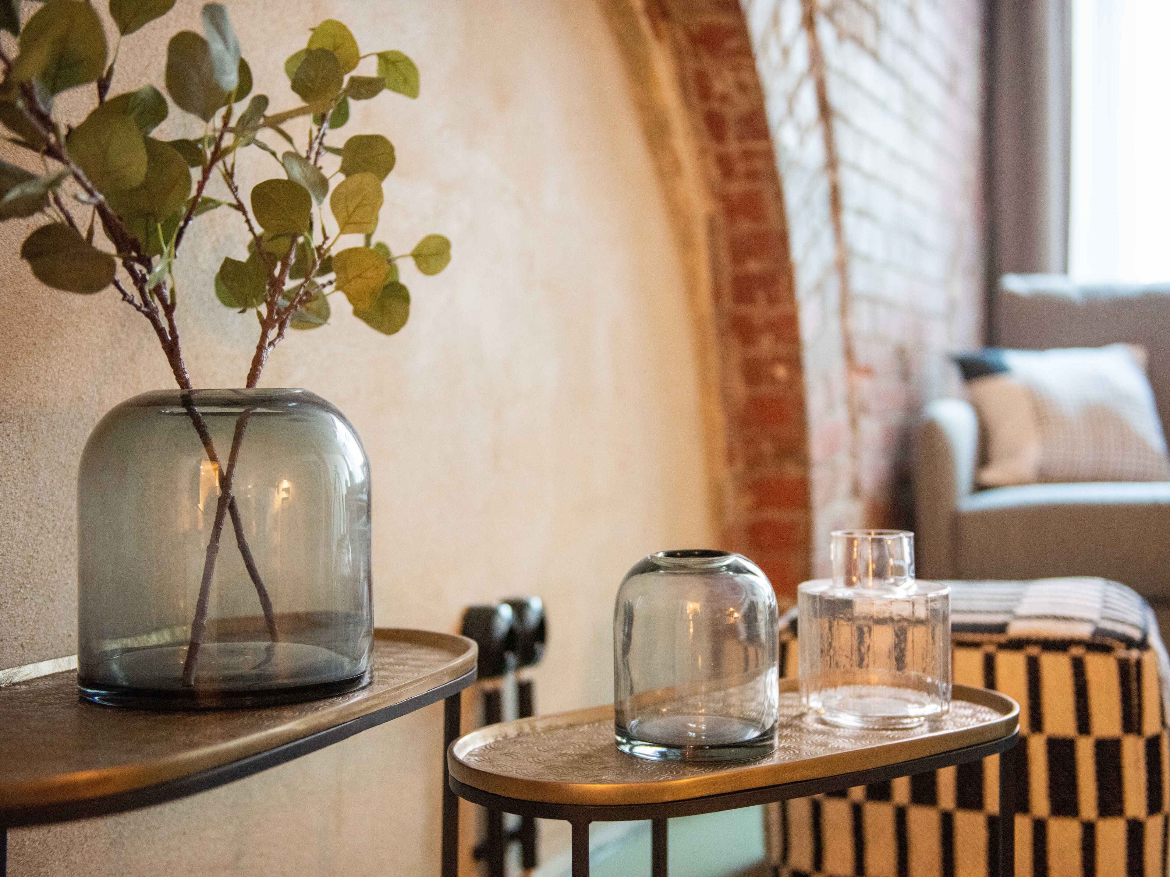Un vase en verre contenant une plante, posé sur une table en bois, un bocal en verre et un verre sur un plateau.