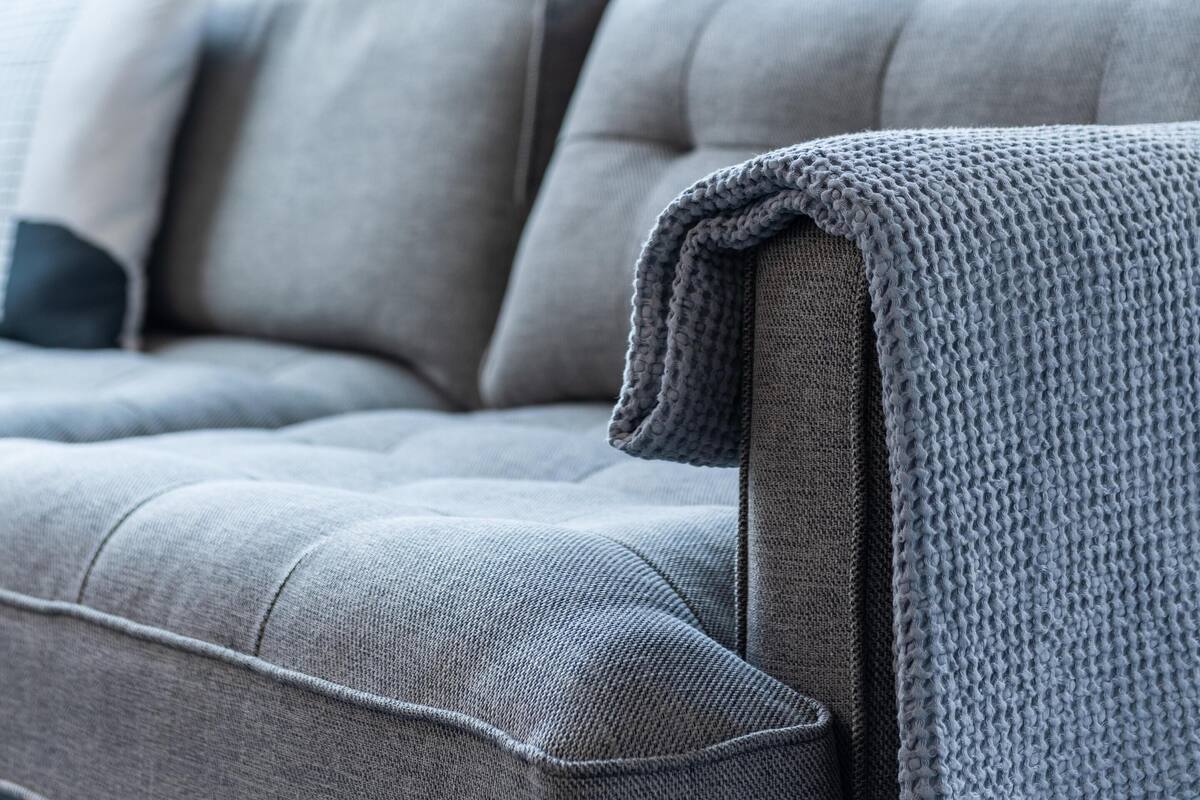 A grey sofa with a knitted throw blanket and a cushion.