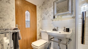 A bathroom with a wooden door, a toilet, a sink with a mirror above it, and a towel rack. - Carnegie Library Bronte Apartment (Swinton)
