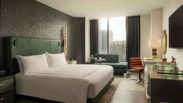 A modern hotel room with a large bed, a desk, a chair, a sofa, and a view of the city.