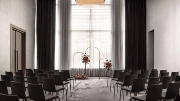 A conference room with rows of chairs facing a large window, a central floral arrangement, and a modern ceiling design.