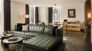 A modern living room with a green leather sectional sofa, a round coffee table, and a dining area with a wooden table and chairs.