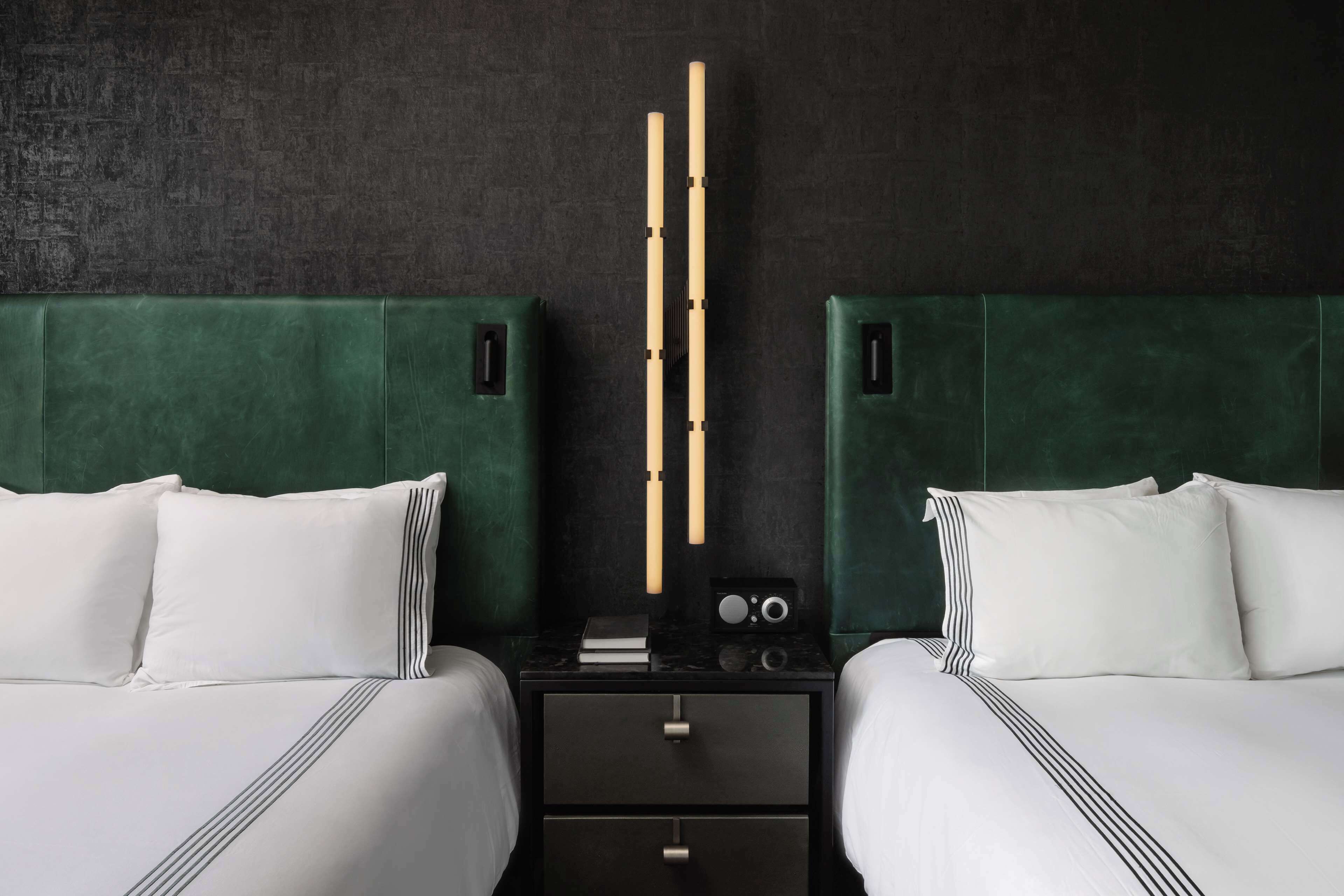 Een hotelkamer met twee bedden, een nachtkastje en een wandlamp.