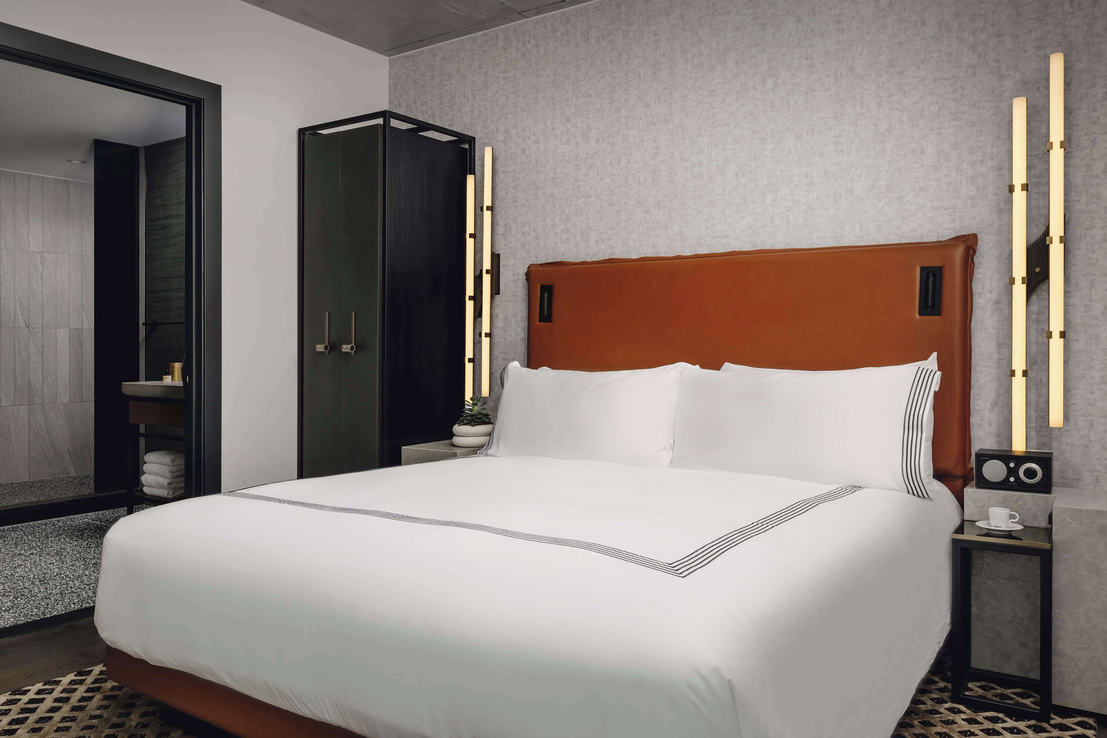 A neatly made bed with white linens and a wooden headboard, a bedside table with a radio, and a mirror on the wall.