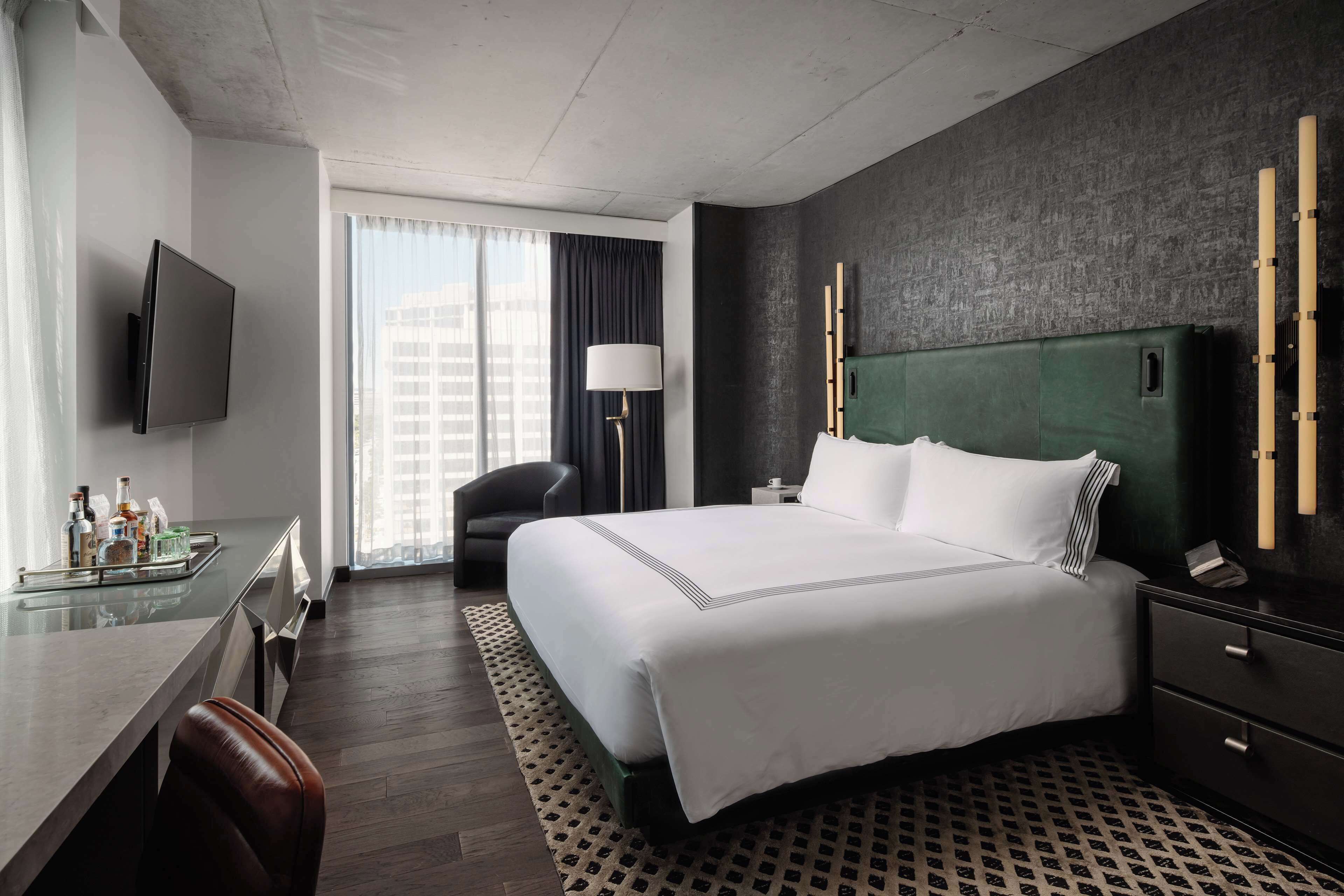 A hotel room with a large bed, a desk with a chair, a TV mounted on the wall, and a window with curtains.
