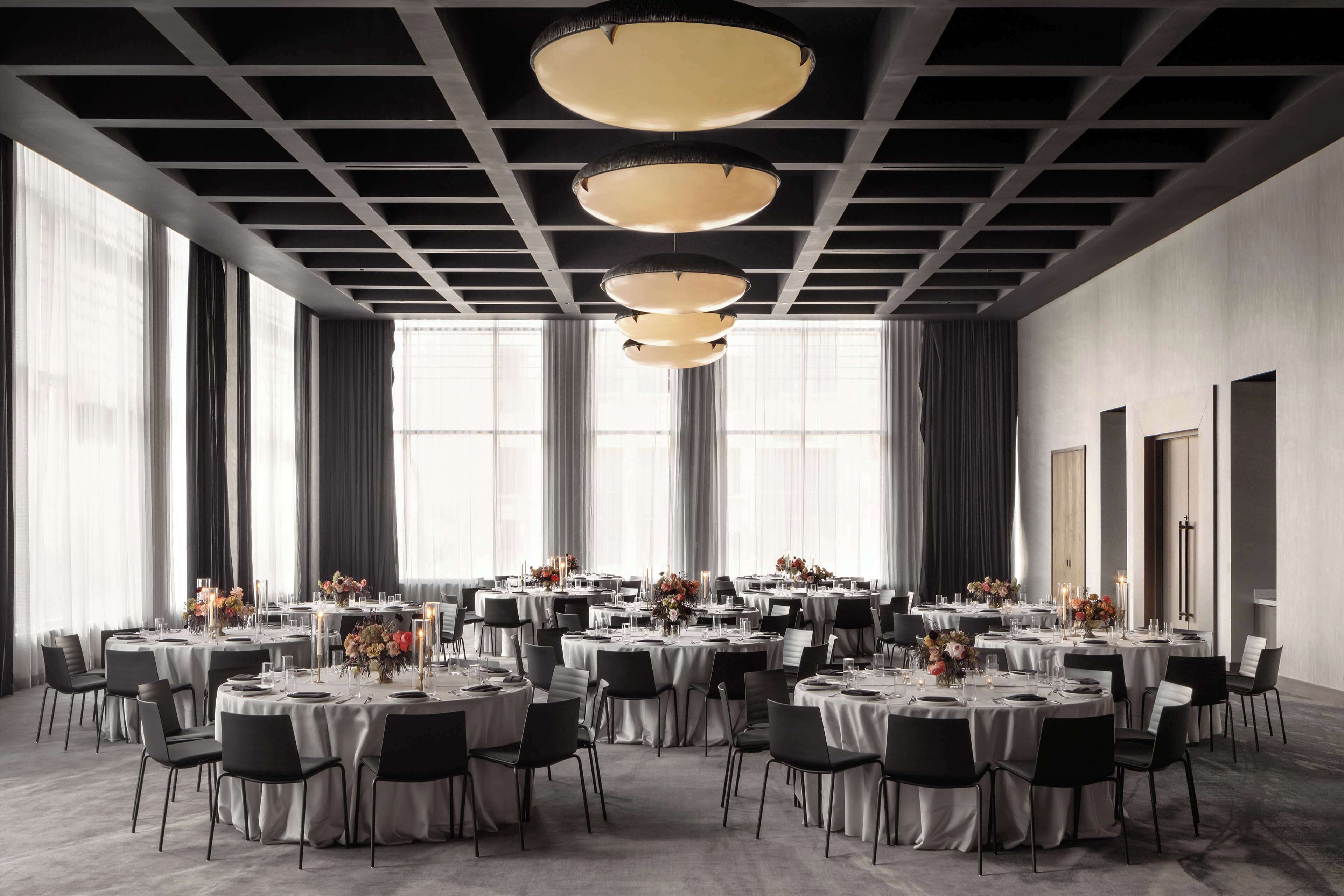 A large, modern conference room with multiple round tables, each set with white tablecloths, black chairs, and floral centerpieces.