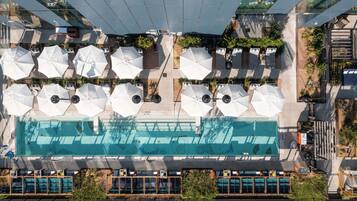 Vista aérea de un hotel con piscina, mobiliario exterior con sombrillas y un diseño arquitectónico moderno.