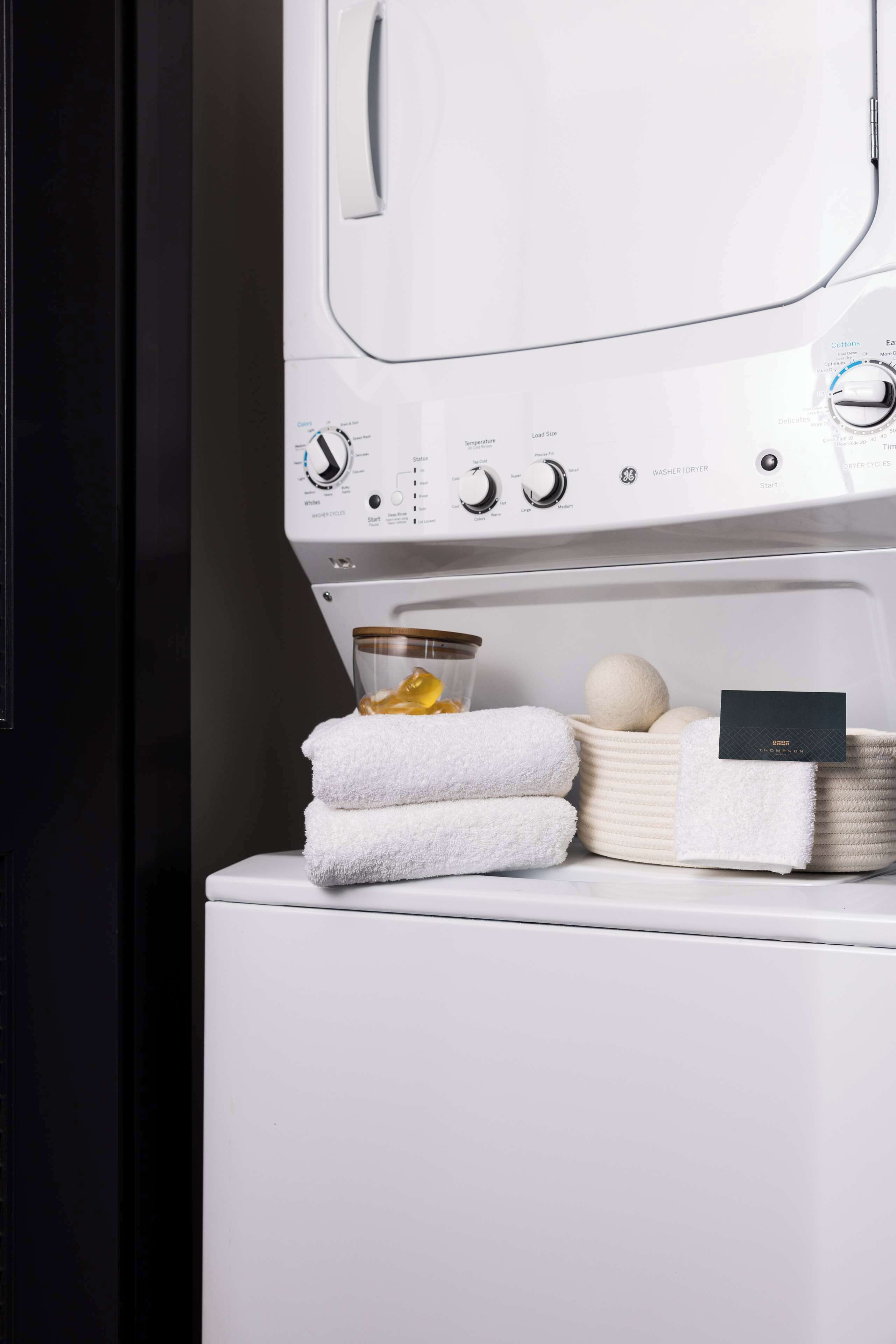 A white washing machine with a control panel, a glass jar with a lemon, and a basket of white towels.