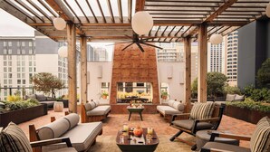 Una terraza en la azotea con mobiliario exterior, chimenea y vistas de la ciudad.