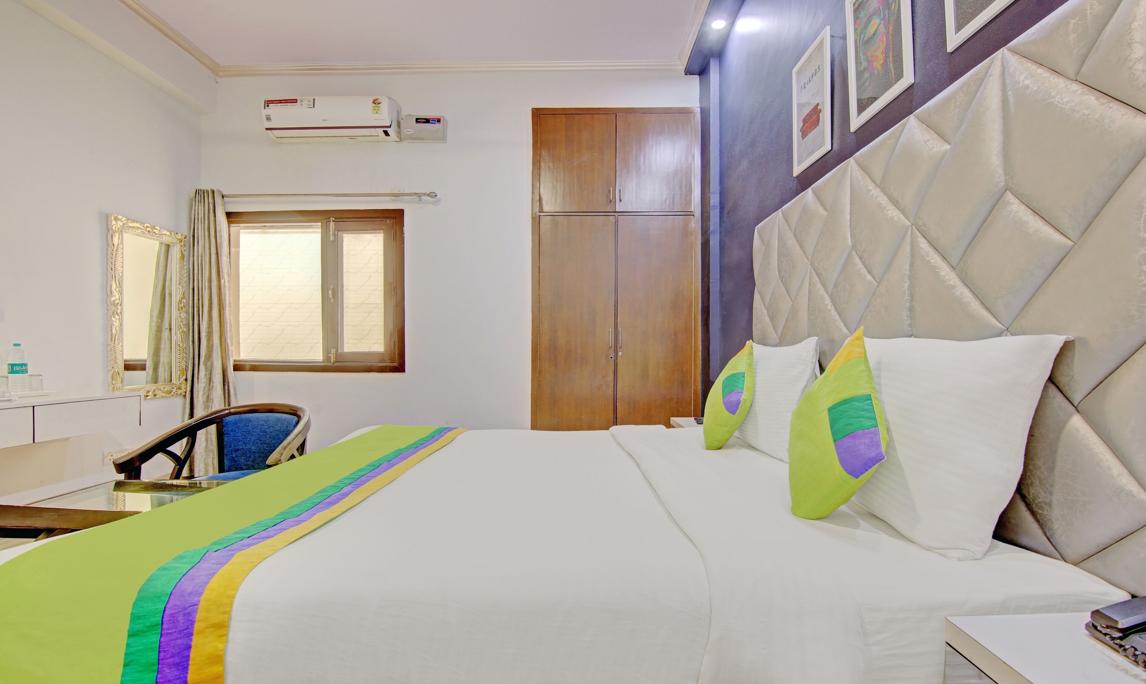 A hotel room with a bed, a desk, a chair, a wardrobe, a window, and an air conditioning unit.