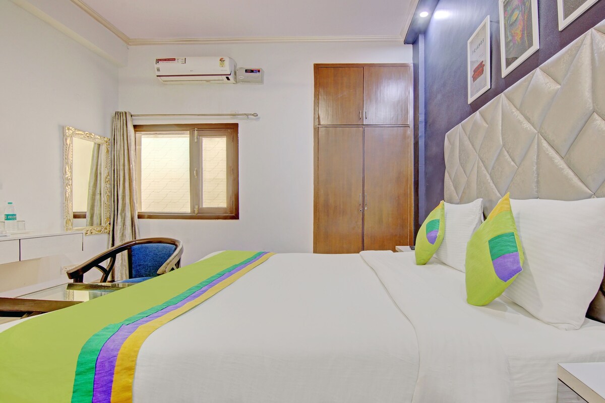 A hotel room with a bed, a desk, a chair, a wardrobe, a window, and an air conditioning unit.