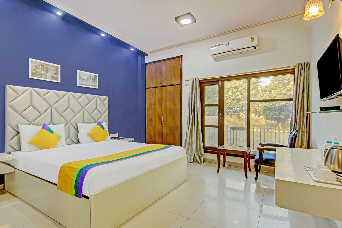 A hotel room with a bed, a desk, a chair, an air conditioning unit, and a window with a view of the outside.