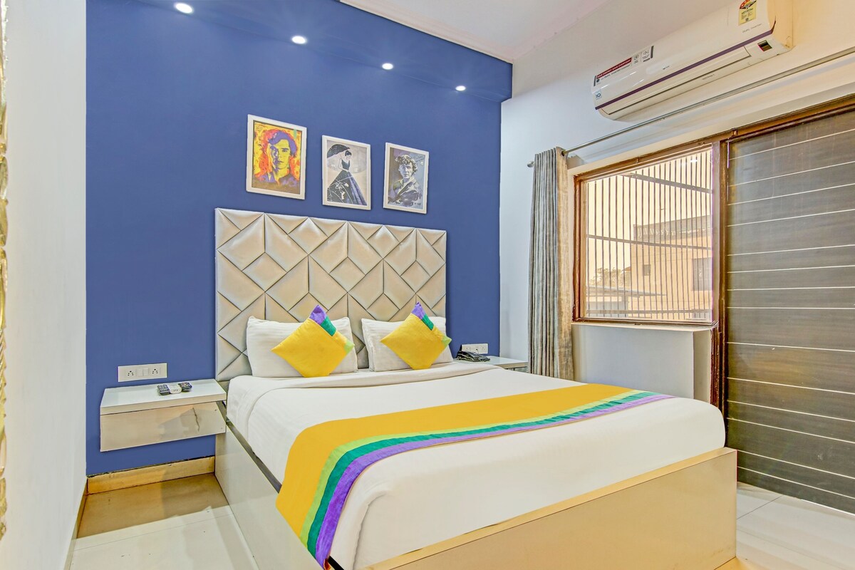 A bedroom with a bed, a nightstand, a window with bars, and three framed pictures on the wall.