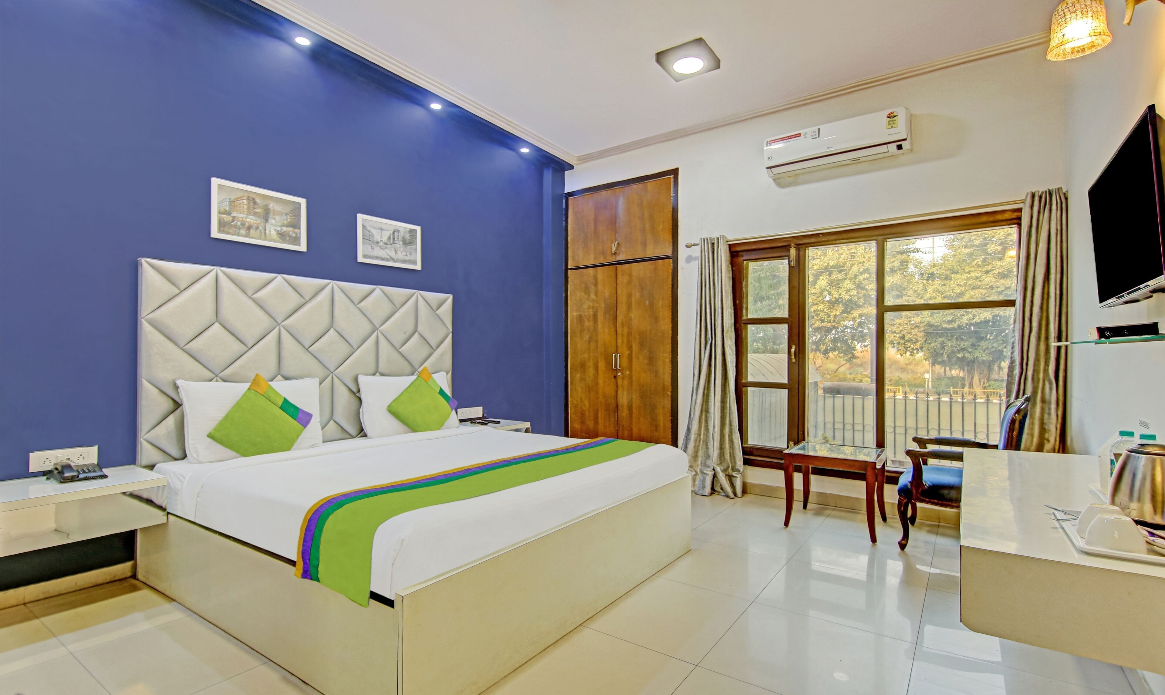 A hotel room with a bed, a desk, a chair, an air conditioning unit, and a window with a view.