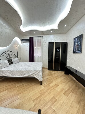 A modern bedroom with a curved ceiling, a bed with a patterned bedspread, a dark bench, and a large painting on the wall. - 3 room apartment on Baghramyan (Yerevan)