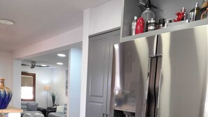 A modern kitchen with a stainless steel refrigerator, a countertop with a bottle, and a dining area with a sofa and table. - Villa de Rêve à 200 Mètres de la Plage de Riells (L'Escala)