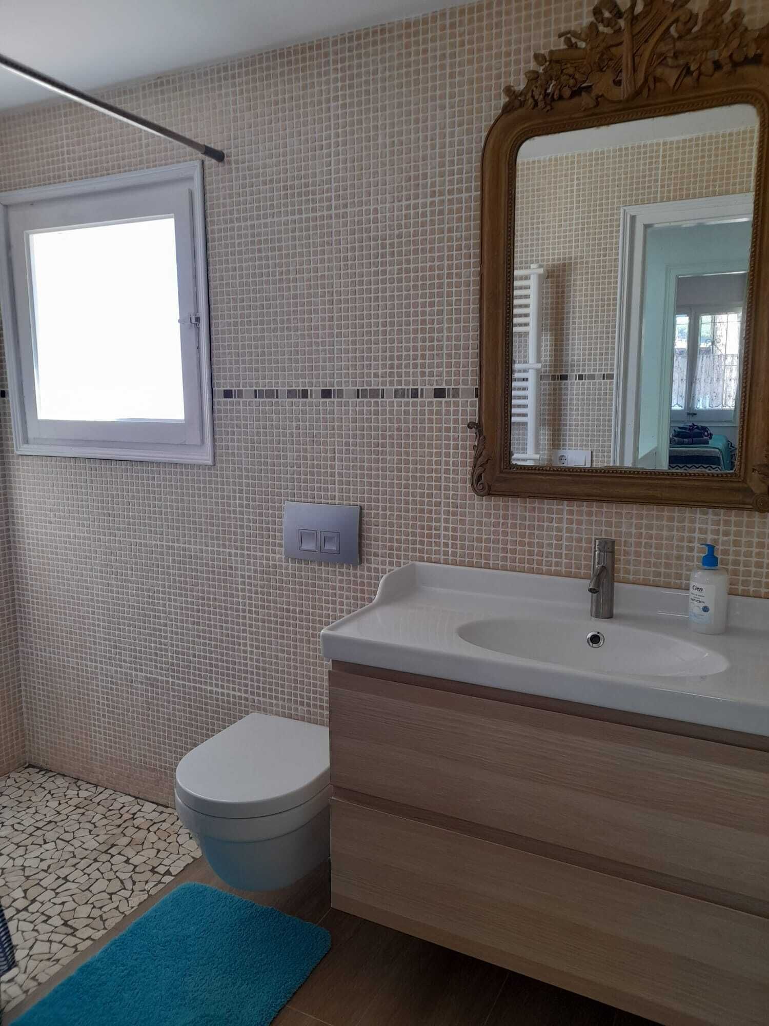 A bathroom with a toilet, sink, mirror, and a window.