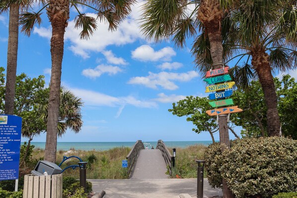 A beach entrance with a wooden walkway leading to the sea, palm trees, and a colorful sign with a message. - ♥ OCEANFRONT VIEW ♥ BEACHFRONT CONDO ♥ NEW ♥ U3 ♥ (Indian Rocks Beach)
