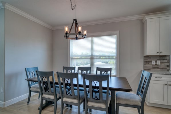 A dining area with a rectangular table and six chairs, a chandelier, and a window with blinds.