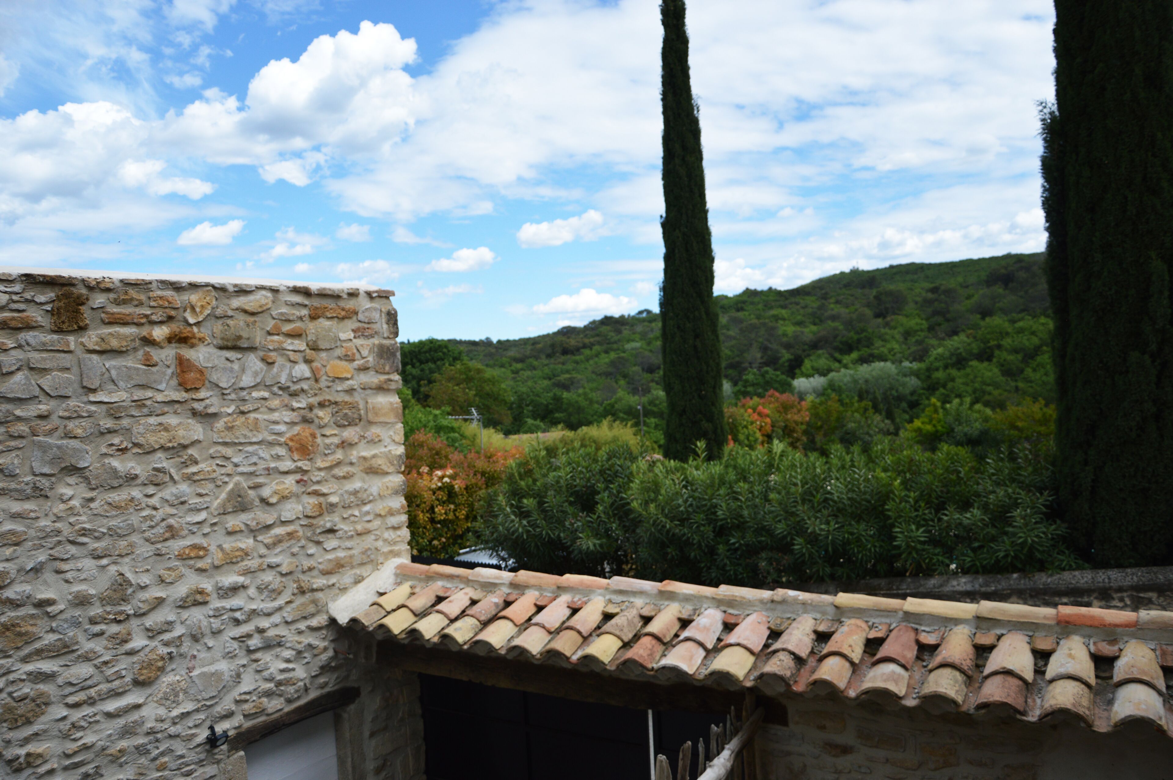 Un bâtiment en pierre, surmonté d’un toit de tuiles, qui domine un paysage verdoyant et luxuriant, parsemé d’arbres et de collines.