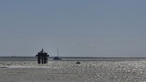 Eine Steg mit einem Gazebogebäude, einer Segelyacht und ruhigem Wasser, das den Himmel spiegelt.