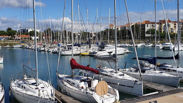 Ein Yachthafen mit mehreren angestaubten Booten, wolkenlosem Himmel und Gebäuden im Hintergrund.