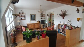 Ein Wohnzimmer mit einer Couch, einem Holzschrank, einem Fernseher und verschiedenen Dekorationselementen, darunter Pflanzen und Figuren.