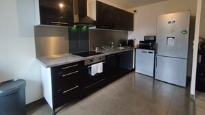 Une cuisine moderne avec des meubles noirs, des appareils en acier inoxydable et un sol carrelé.